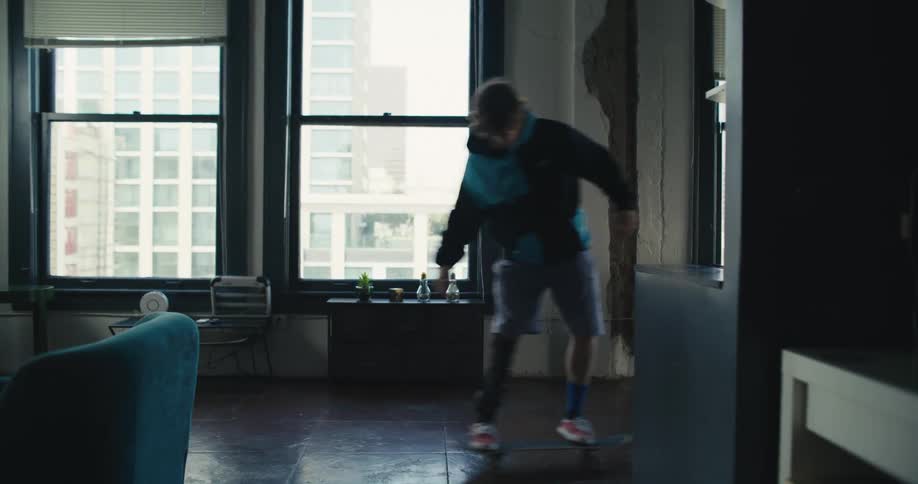 A teenage boy with an artificial leg skateboards through a house