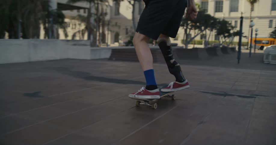 A teenage boy is riding his skateboard through a park and he does a kick flip stunt and then does a 180 degree turn as he leaps over stairs
