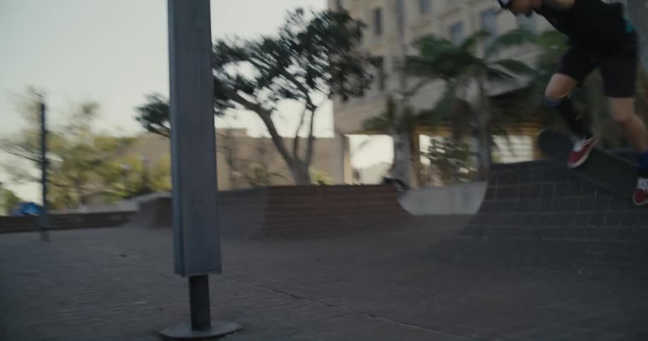 A teenage boy is riding his skateboard through a park and he falls on his rear end trying a stunt