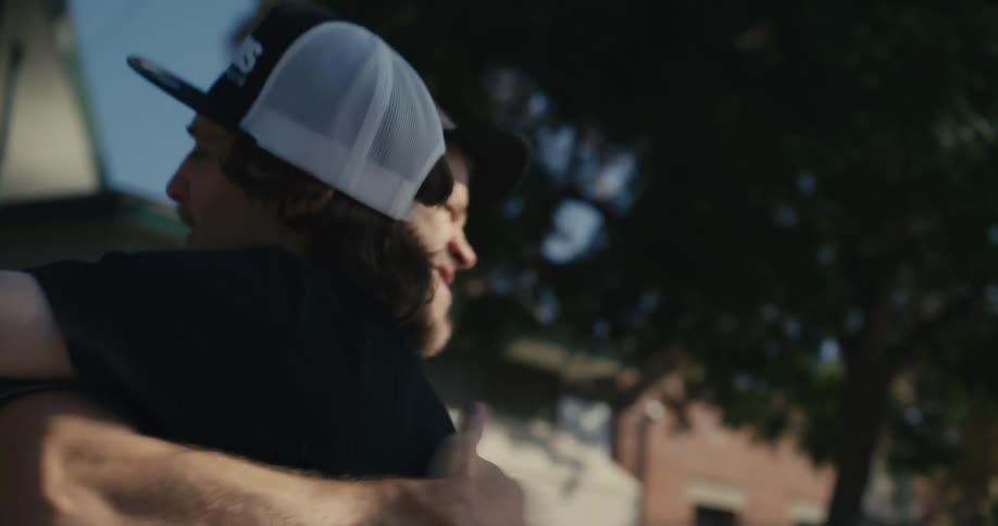 Two men greet each other with a handshake and a hug on the sidewalk