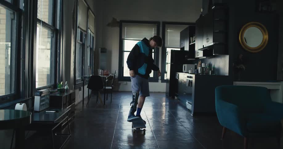 Man wearing a prosthetic brace balances on skateboard in apartment