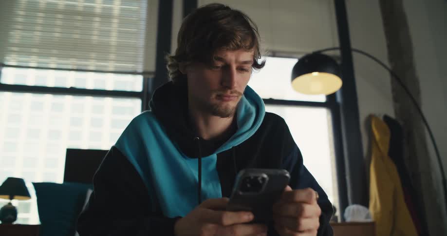 Young man scrolling through his cell phone in his bedroom