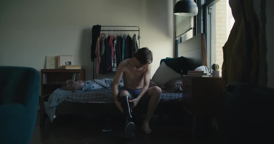 A man sits on a bed and puts his prosthetic leg on
