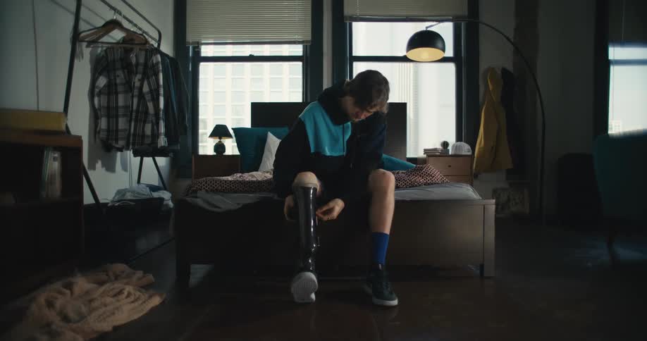Man sitting at foot of bed puts on prosthetic leg