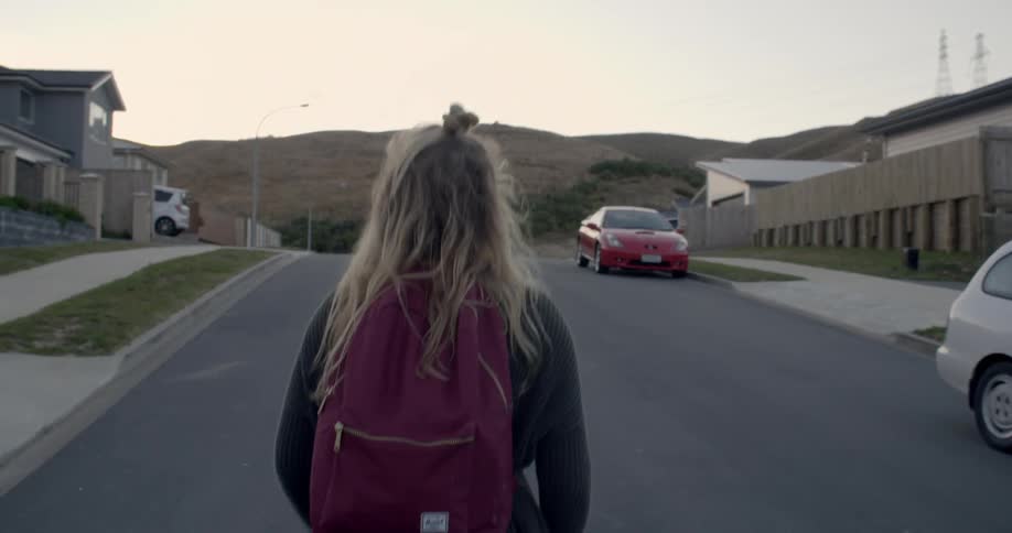 Girl with backpack walks down a neighborhood road