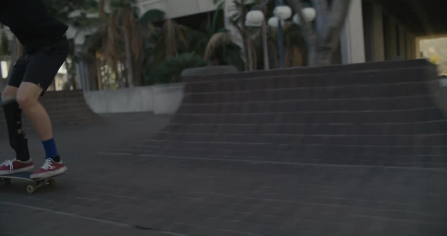A man with a prosthetic leg skateboards and grinds up a small ramp by a tree