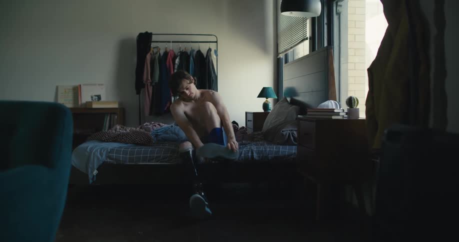 A man in a leg cast gets dressed in his bedroom