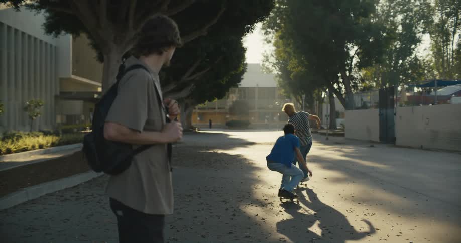 A man crossing the street is interrupted by skateboarders who he watches as they pass by