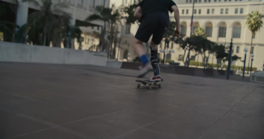 A teenager in a leg cast does skateboarding stunts through downtown