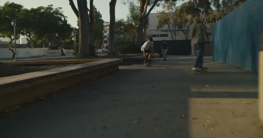 Teenage boys are riding skateboards through a park and doing stunts