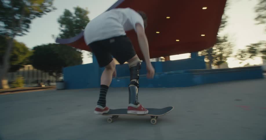 A man with a prosthetic leg skateboards on the concrete and falls after attempting a trick