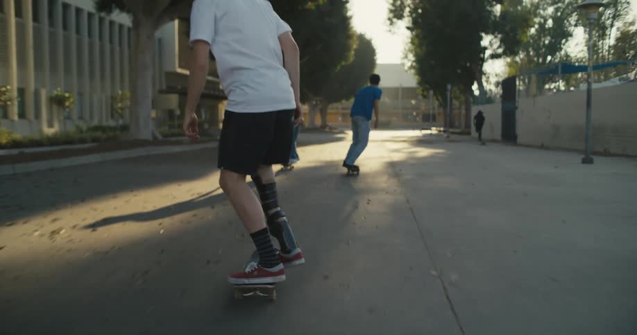 Skateboarding friends follow each other along pavement and try to perform tricks