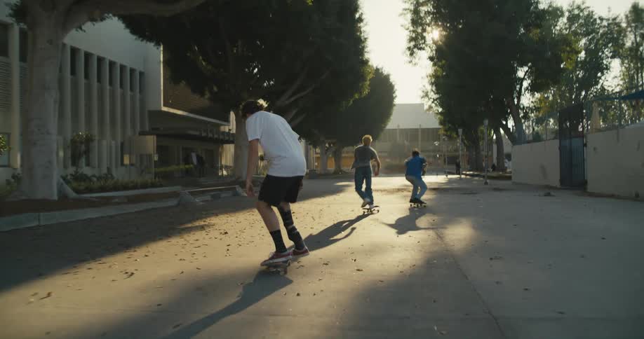 Teenagers skateboard down a pathway at a park during the day