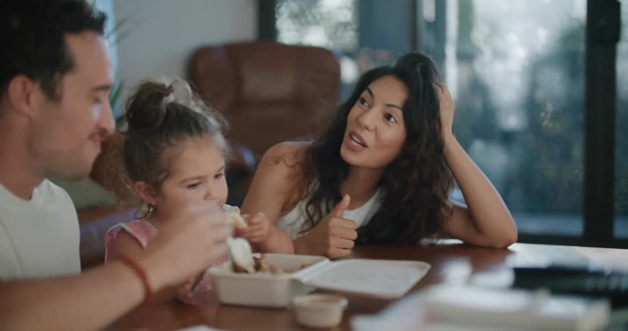 A mother and father sit at a table with their toddler daughter eating