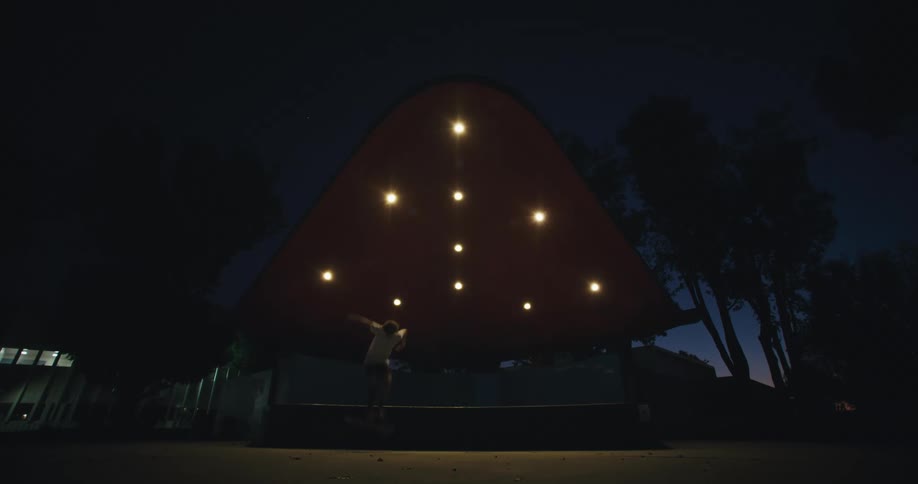 Male skateboarder jumps off platform under pavilion at park at night