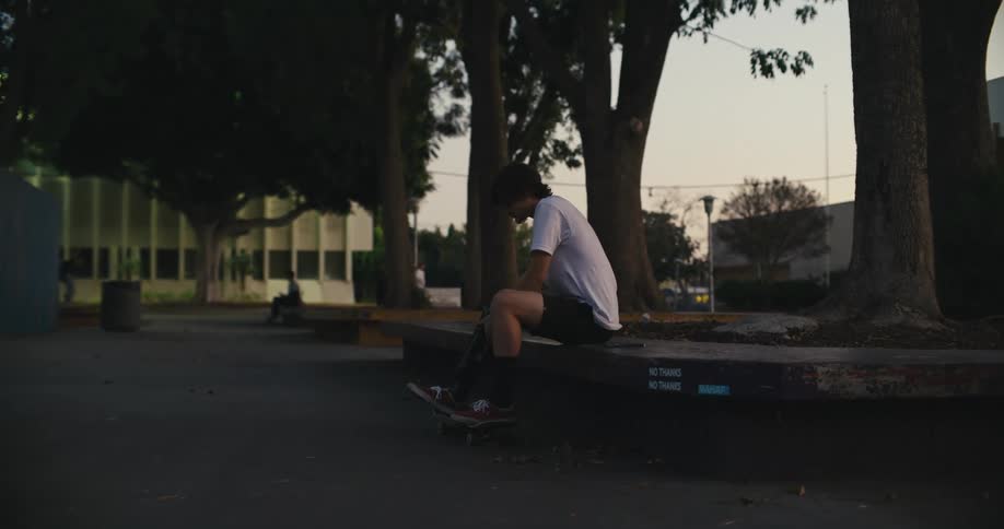 A man adjusts his prosthetic leg while sitting under a large tree in a park