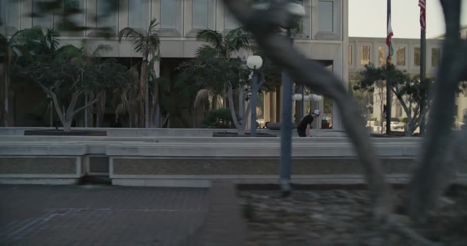 Skateboarder jumps skateboard down steps as he rides toward street crossed by enclosed pedestrian bridge