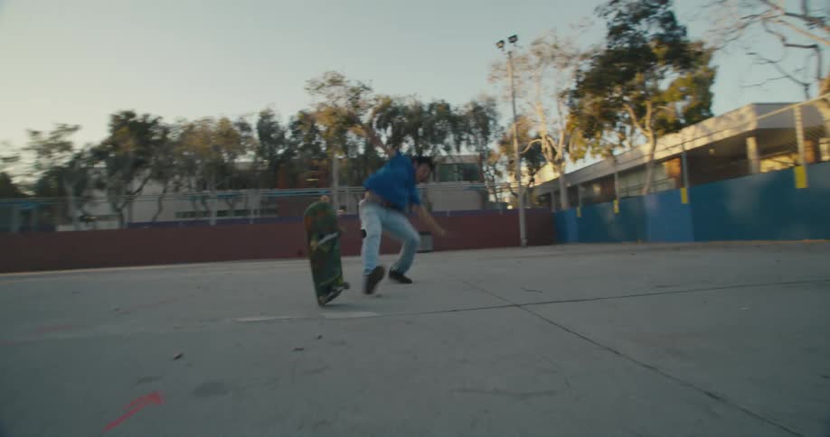 Skateboarder in park tries to perform jump trick and falls and fellow skateboarders clap