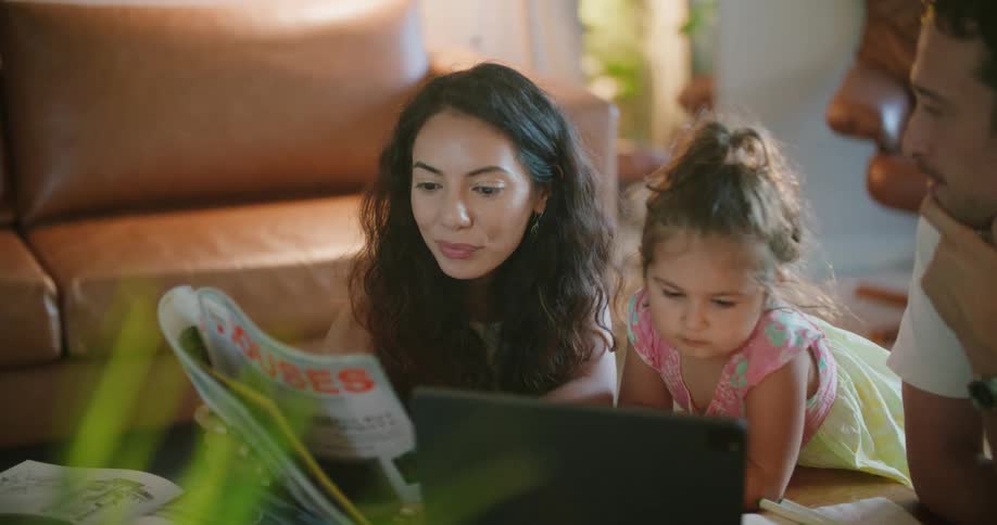 A couple read a magazine together while their daughter plays on a tablet