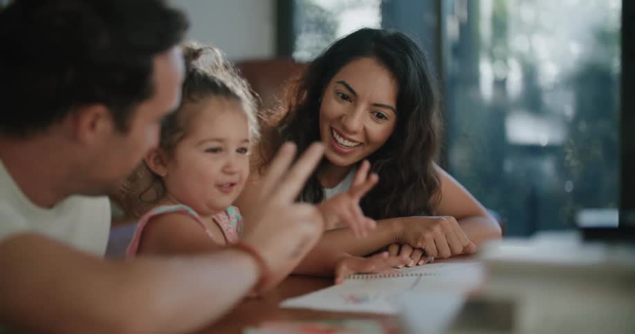 A woman and man sit at a table with a toddler girl helping her count