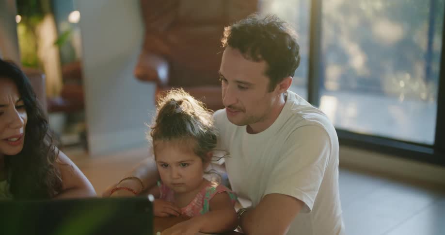 A mother and father sit with their toddler daughter in front of a tablet