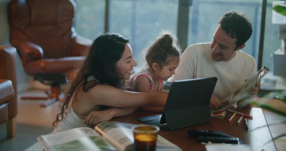 Parents sit with daughter near laptop as they look through book