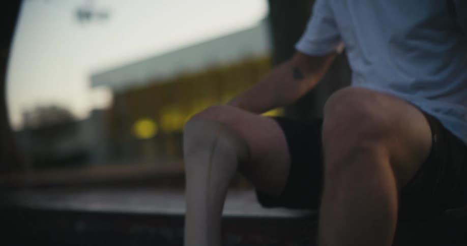 A man adjusts and straps on his prosthetic leg while sitting on a park bench
