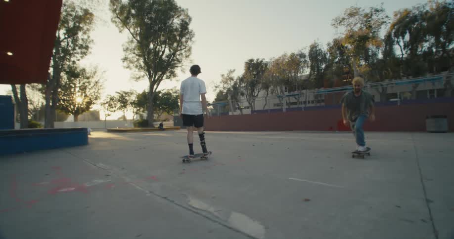 Two skateboarders one with wearing a prosthetic perform jump tricks on a skateboard