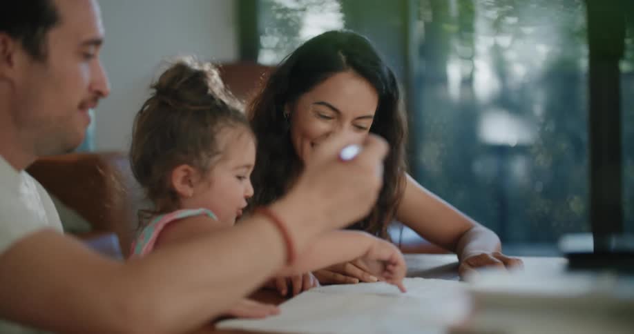 A family laughs as they draw together at home for their daughter