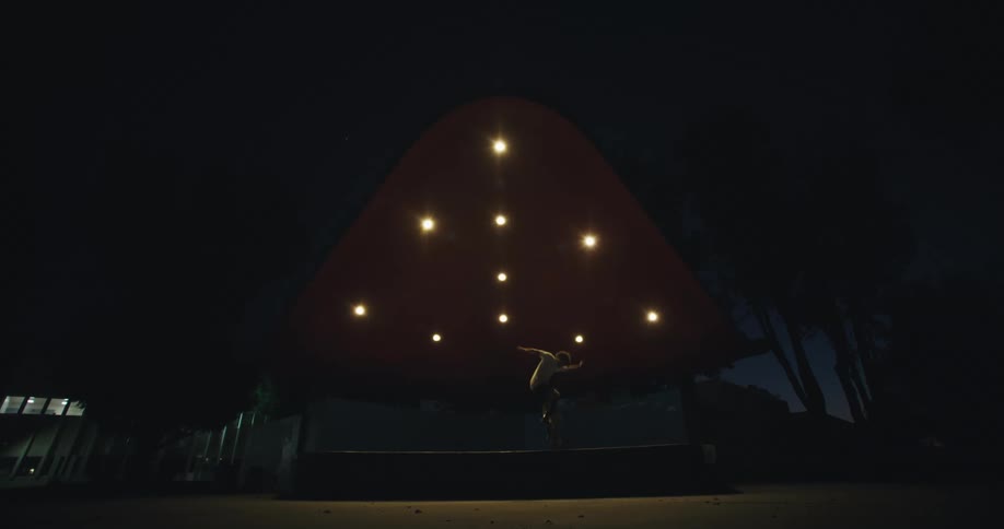 Skateboarder jumps off pavilion at park at night and falls