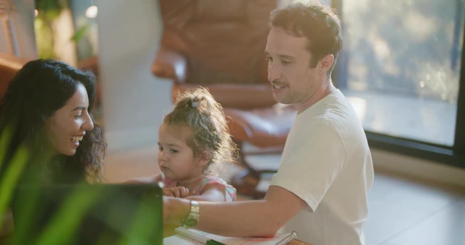 Parents sit on floor in living room with daughter discussing contents shown on laptop screen