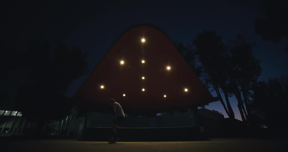 A male on his skateboard jumps off a ledge in a public park at night