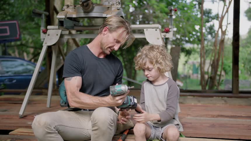 A man shows his son how to use a drill at home