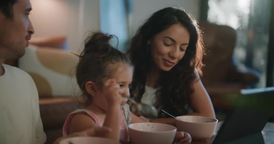 A family chats as they eat a meal out of bowls while sitting on the floor