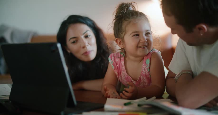 A man gives his daughter an eskimo kiss while she laughs watching something on a laptop
