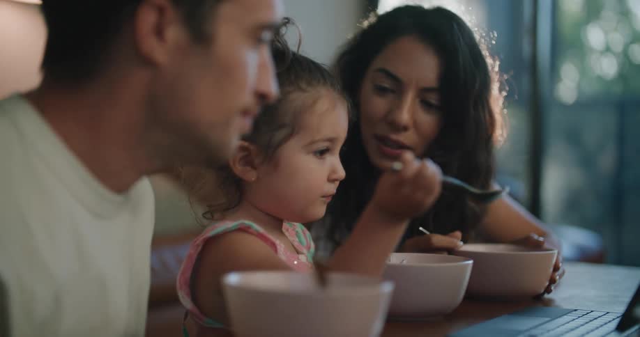 Parents and daughter discuss laptop contents as they eat at the coffee table