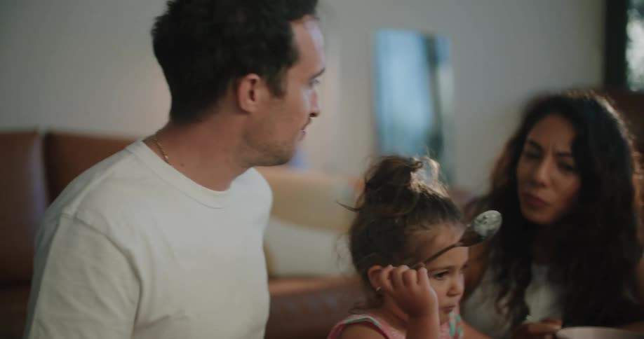 A man and woman sit with a young girl eating and watching a tablet screen