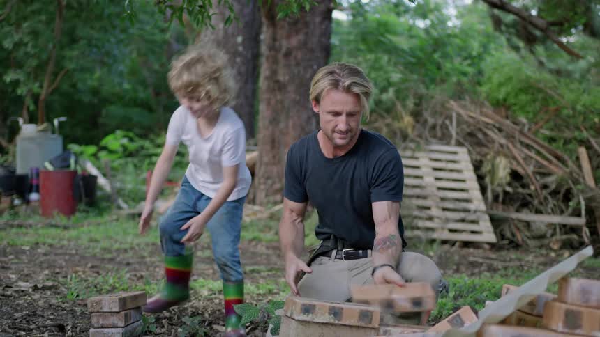 A father and son stacking bricks in a garden