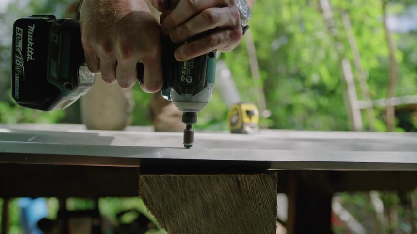 A man drills a screw through a piece of plywood outdoors