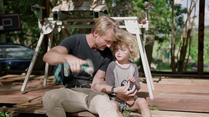 A man talks to his son about power tools as they sit on a deck