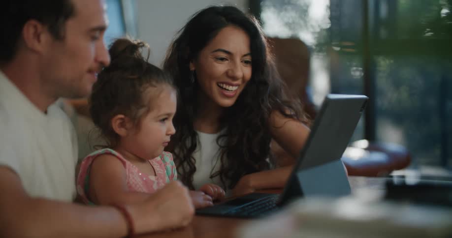 Parents sit near daughter as they watch monitor sitting on coffee table
