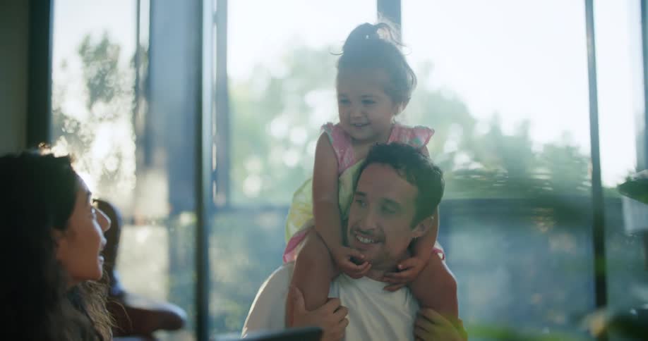 A family sit together at a table with the daughter on the fathers shoulders