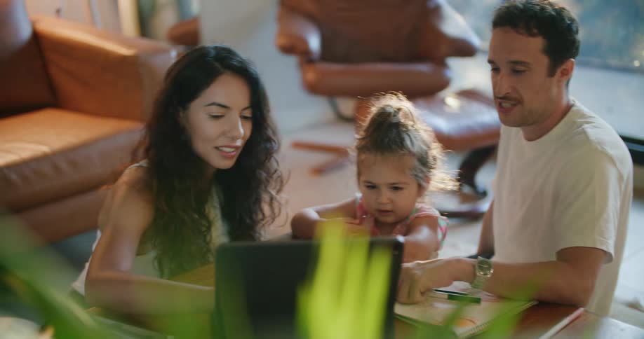 Father with mustache and mother with wavy hair help daughter using tablet at coffee table in living room at home
