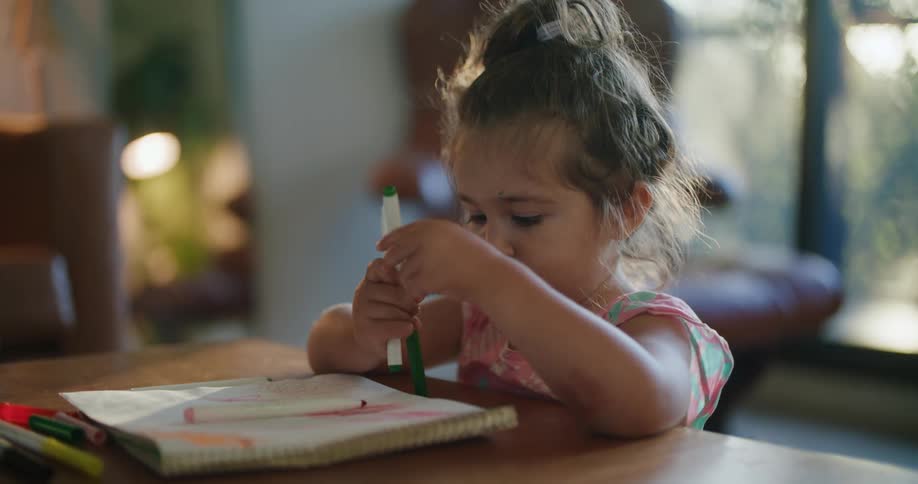 A girl looks at markers while drawing at home
