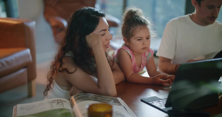 A man sitting next to his daughter and wife flips through a magazine while they look at a laptop