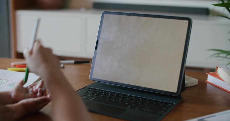 Mother with wavy hair plays with her daughter sitting at coffee table next to tablet with white screen in living room at home