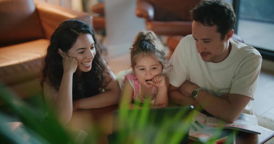 Father with mustache white t shirt and mother with wavy hairand toddler girl watch tablet on coffee table in living room at home