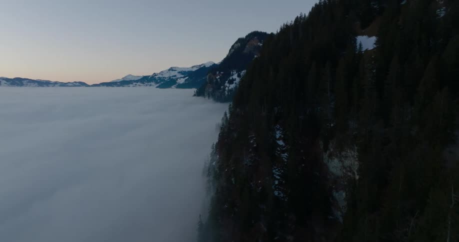 A thick layer of cloud covers a valley with snow covered mountains surrounding
