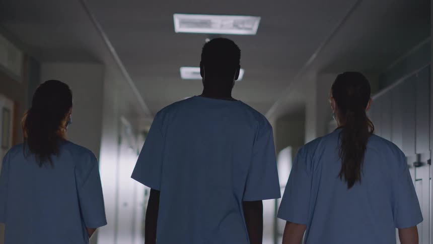 Three nurses walk down a corridor all wearing scrubs and masks