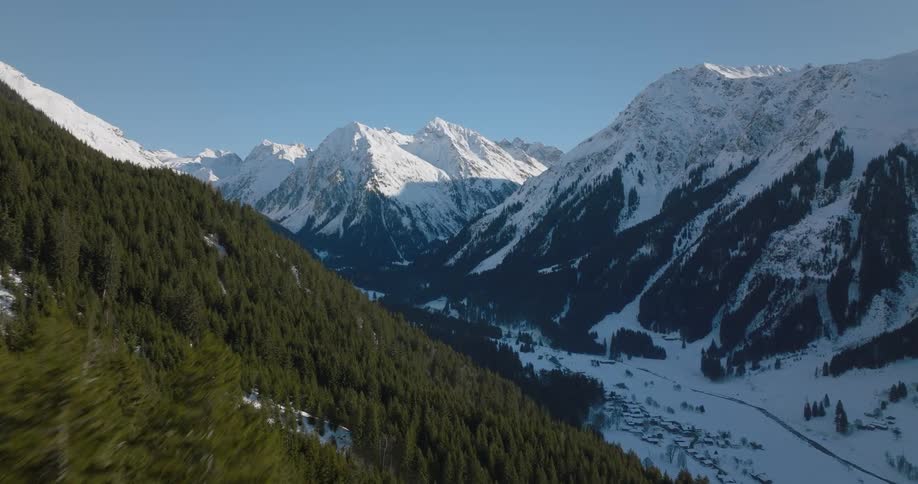 Snow covered town sits in shadowed valley between conifer covered slopes